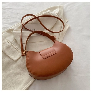 Borsa a sella marrone a mezzaluna con fibbie dorate su sfondo di un blazer neutro
