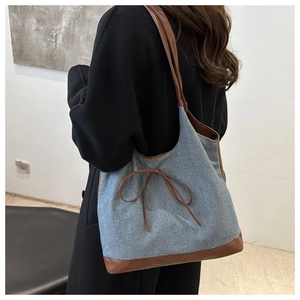 Vista laterale della grande borsa tote in denim con finiture in pelle su cappotto nero