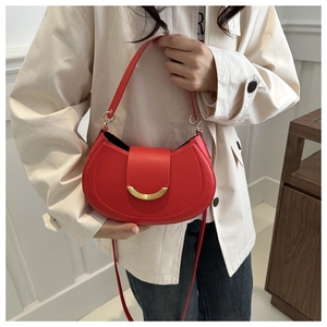 Dettaglio borsa a mezzaluna in pelle rossa con chiusura dorata su sfondo cappotto bianco