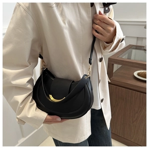 Dettaglio di una borsa a tracolla nera a mezzaluna con fibbia dorata su un trench beige