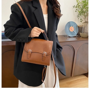 British style brown faux leather satchel bag worn by a model in a warm interior setting