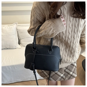 Black leather tote bag with white contrast stitching styled on a beige cable-knit sweater