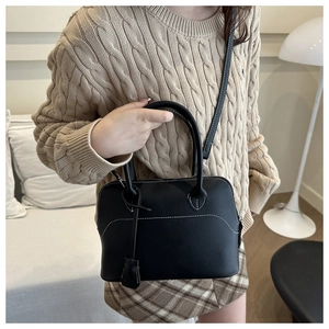 Detail of black vintage matte leather handbag with white stitching and leather bell charm