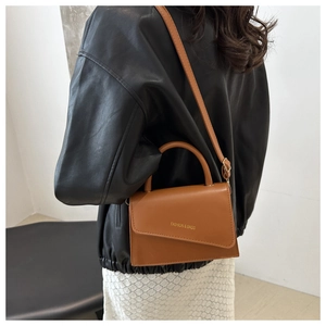 Detail of tan crossbody bag with asymmetrical flap and gold fashion text design