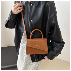 Close-up of brown crossbody bag with asymmetric flap and golden fashion logo on leather jacket