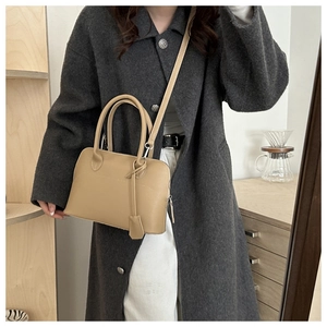 Niche stylish light khaki tote bag with top handle and adjustable strap worn on coat