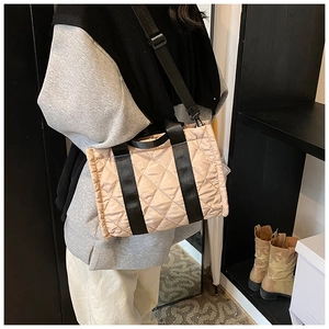 Detail of light beige quilted tote bag with black strap worn as a crossbody bag