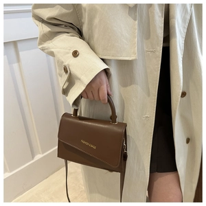 Detail of dark brown leather handbag with asymmetric flap and golden text branding