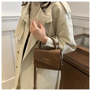 Brown leather crossbody bag with asymmetrical flap shown on a trench coat outfit