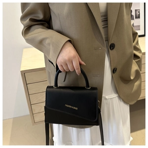 Chic black minimalist handbag worn with a stylish blazer and pleated white skirt