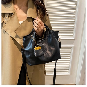 Detailed view of a black leather tote bag with a gold chain mini charm on a trench coat