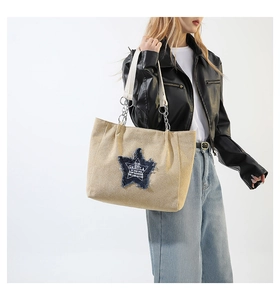 Detail view of beige canvas tote bag with denim star patch and metal chain strap