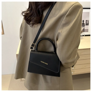 Detail of black leather handbag with asymmetrical flap and gold fashion text on top