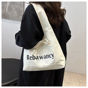 Detail of cream canvas hobo bag with side bow tie and black letter print on strap