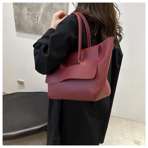 Modell mit großer weinroter Ledershoppingbag mit asymmetrischer Klappe über schwarzem Mantel
