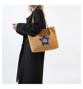 Detail of tan faux suede tote bag featuring a denim star patch and metal chain strap