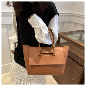 Detail of the unique brown leather tote bag handle structure and matte texture on model