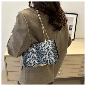 Détail d'un sac bandoulière léopard avec chaîne dorée porté sur un blazer marron