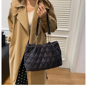 Close-up of a large black quilted tote bag being carried by a model in a trench coat.