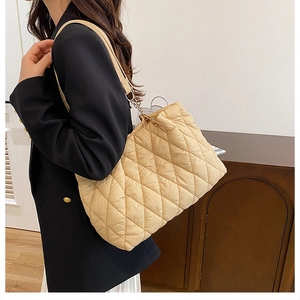 Vista laterale di una borsa tote trapuntata beige indossata da una modella in interno