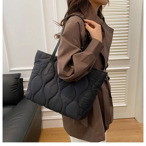 Détail d'un sac cabas matelassé noir avec coutures ondulées porté par un mannequin en manteau