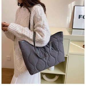 Sac cabas gris matelassé avec coutures ondulées porté par un mannequin en intérieur