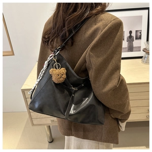 Detail of black faux leather tote with plush bear charm and silk scarf on strap