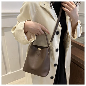 Detail of brown leather bucket bag with gold clasp and fashion logo on beige trench coat
