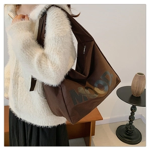 Vista laterale della borsa tote in tela marrone scuro con scritta MOOD e giacca bianca
