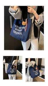 Detail of blue denim tote bag featuring white slogan print and plush bear keychain charm