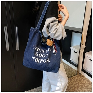 Detail of blue denim tote bag with white text print and cute brown teddy bear charm