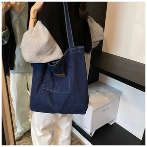 Close-up of deep blue denim tote bag featuring external pocket and leather patch detail