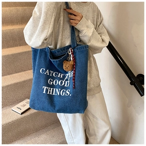 Detail of blue denim tote bag with text print and a cute brown plush bear charm