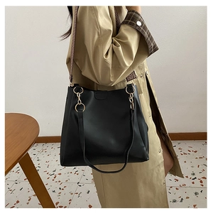 Detail of black tote bag featuring a geometric woven strap and gold ring hardware