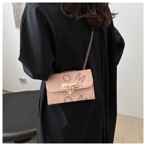 Pink leather crossbody bag featuring gold heart lock and chain strap on a black dress