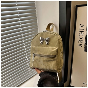 Detail of mini nylon backpack in light khaki featuring a silver metal bow and front pocket