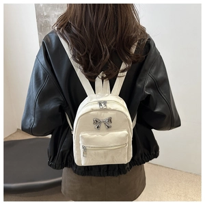 Detail of white mini backpack with silver metal bow and textured PU leather surface