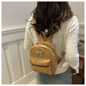 Close-up of ginger yellow bow backpack with pleated texture and silver hardware details
