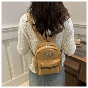 Close-up of khaki mini backpack with pleated texture and silver bow metal detail
