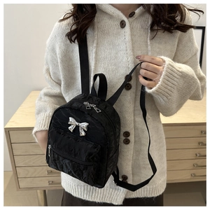 Detail of black mini backpack with silver bow accent and adjustable straps on a model
