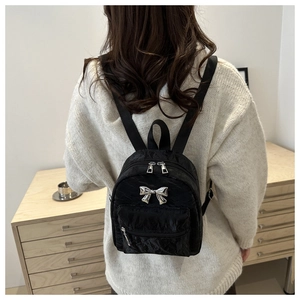 Chic black pleated mini backpack featuring a silver metal bow accent and adjustable straps