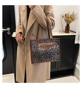 Detail of leopard print tote bag featuring brown leather trim and metal zipper accent