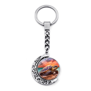 Close-up of rotating sea turtle pendant keychain with crescent moon and sunset beach design