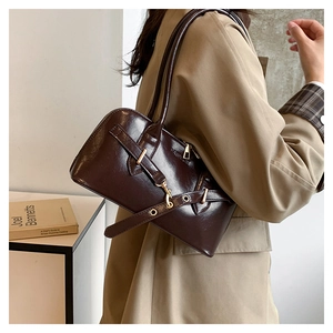 Close-up of a dark brown glossy leather Boston bag with gold buckles and chic strap
