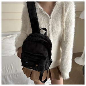 Close-up of black fuzzy plush mini backpack with colorful buttons on a female model