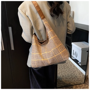 Detail of plaid tote bag with wide brown leather strap on model in cozy home setting