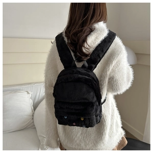 Detail eines weichen schwarzen Plüschrucksacks mit bunten Punkten auf einem Strickpullover