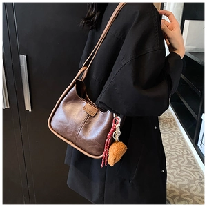 Detail of vintage brown oil wax leather shoulder bag with contrast piping and bear charm
