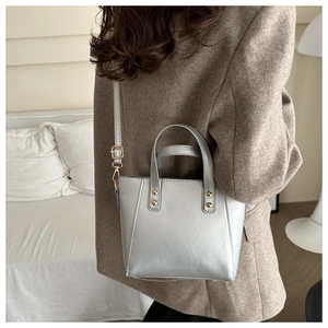 Sac fourre-tout argenté avec rivets dorés porté en bandoulière par un mannequin