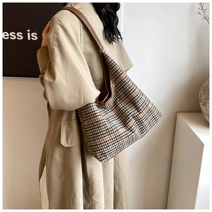 Close-up of retro plaid wool tote bag with brown leather strap worn with beige trench coat